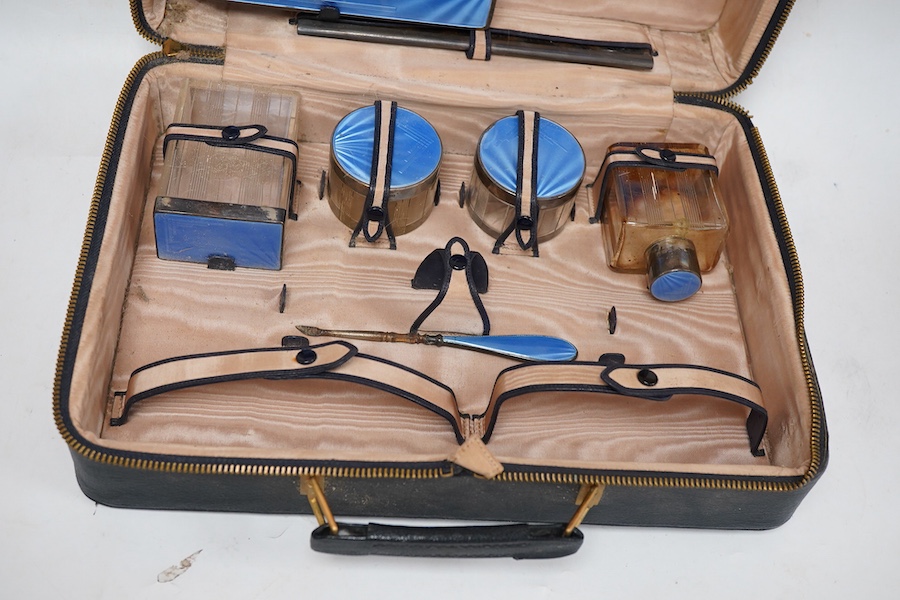 A George V/George VI Art Deco vanity case containing nine silver and blue guilloche enamel mounted items including a hand mirror, brushes, nail implement etc. Walker & Hall, 1936/37, incomplete.